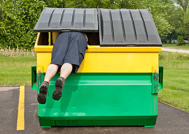 person hanging outside a large dumpster